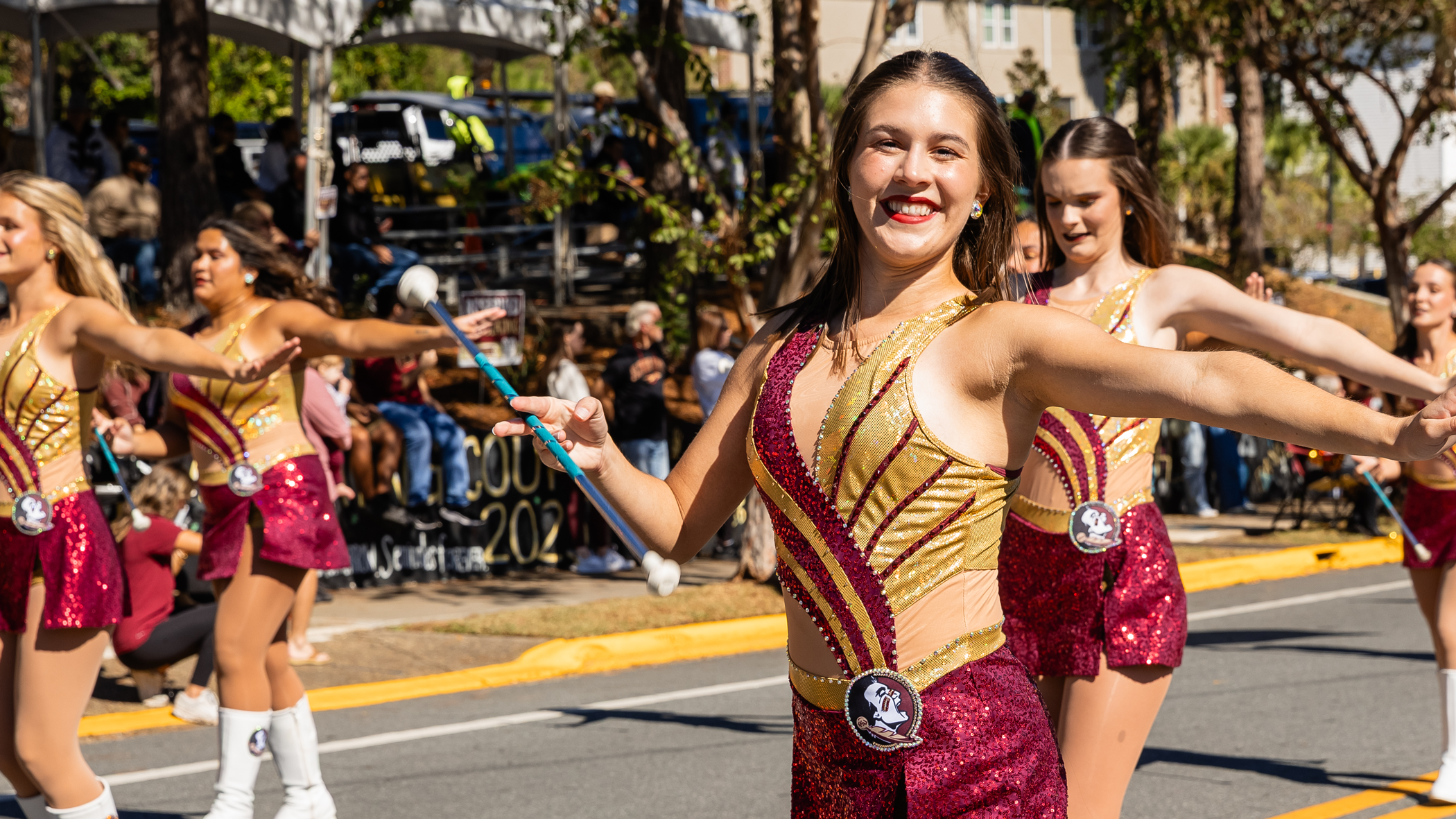 A photo of FSU majorettes performing in a homecoming parade, one looking at the camera and smiling while twirling a baton