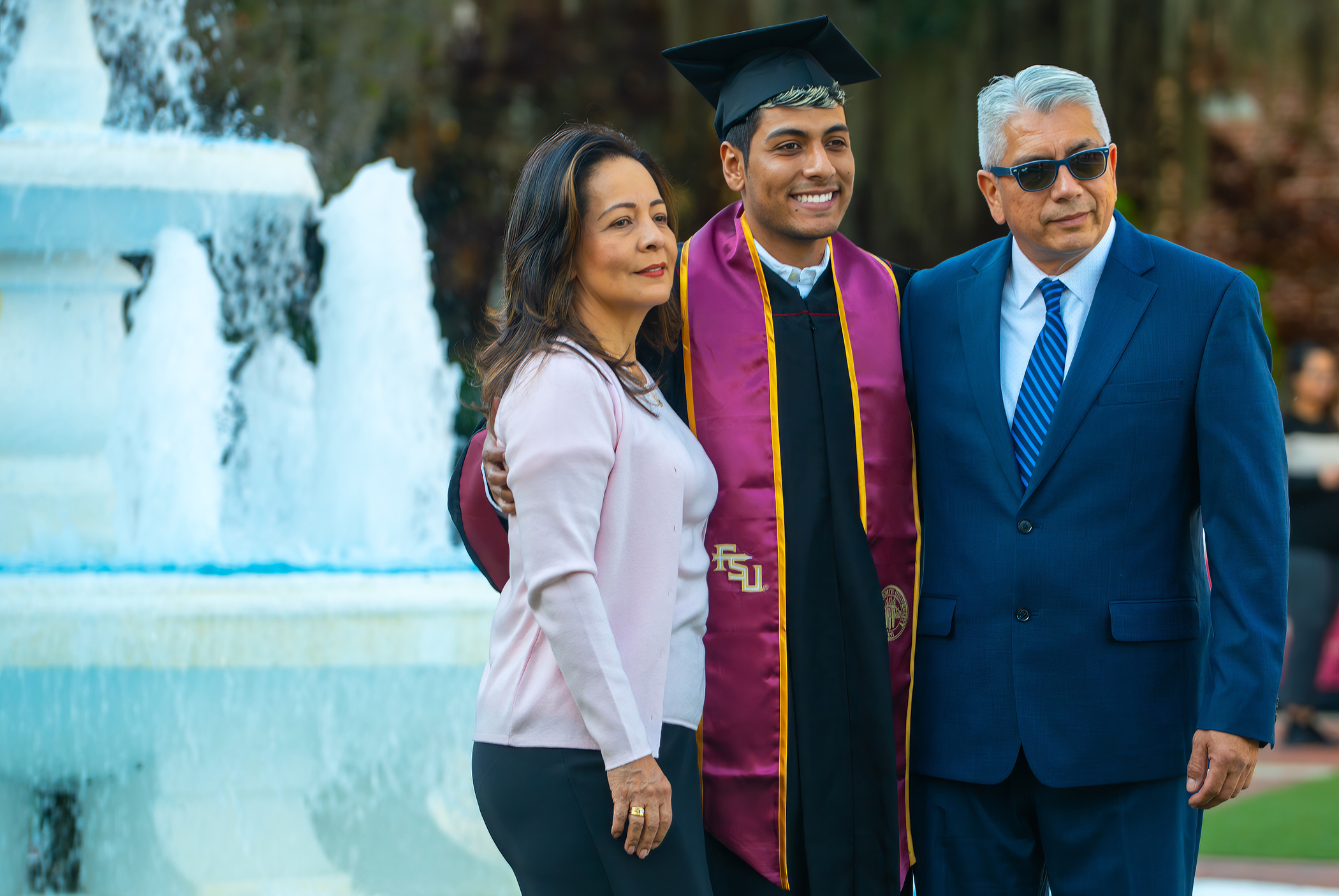A photo of a mother and father posing with their son in his cap and gown